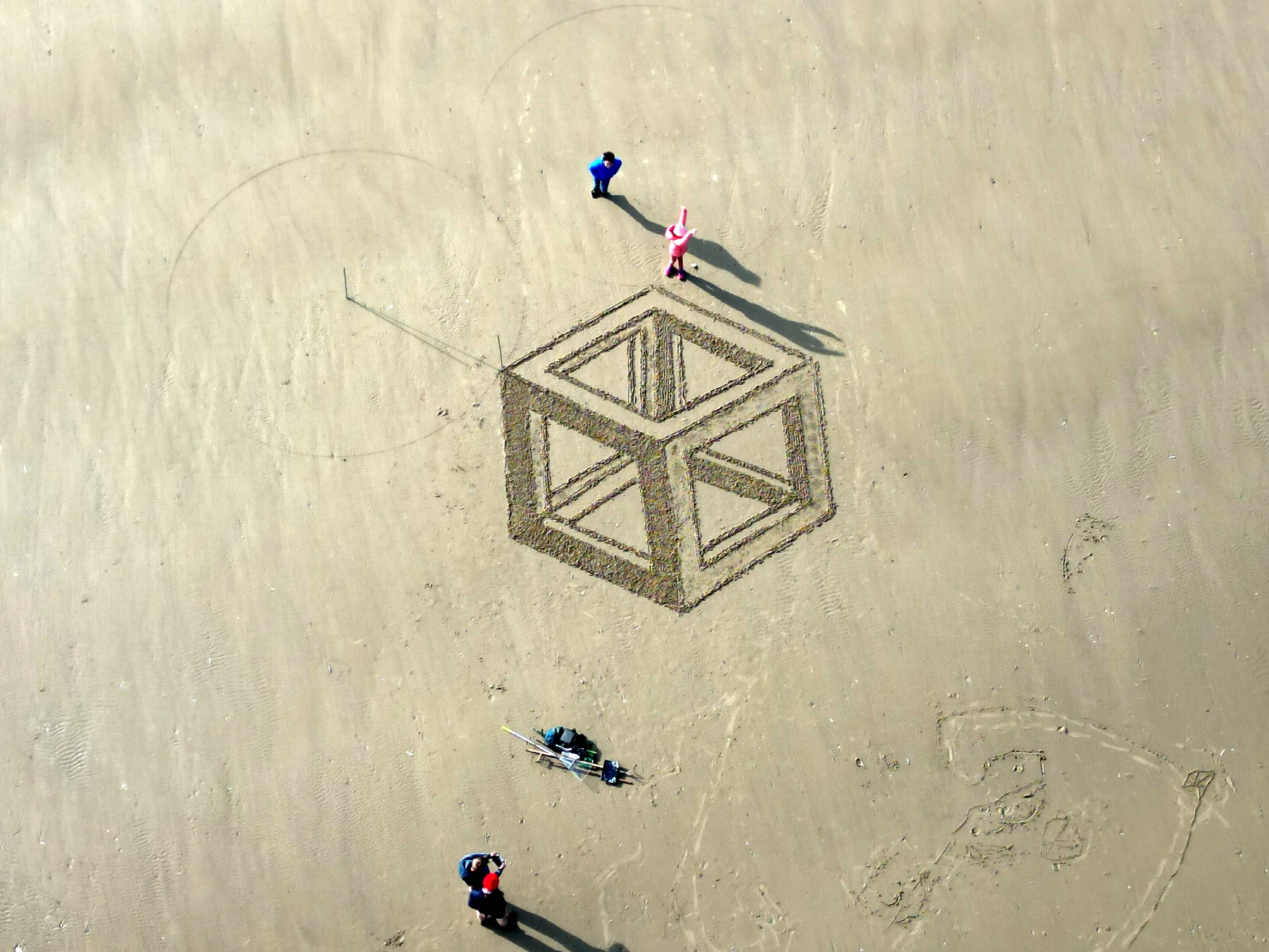 Vue rapprochée d’une construction géométrique tracée dans le sable avec plusieurs personnes