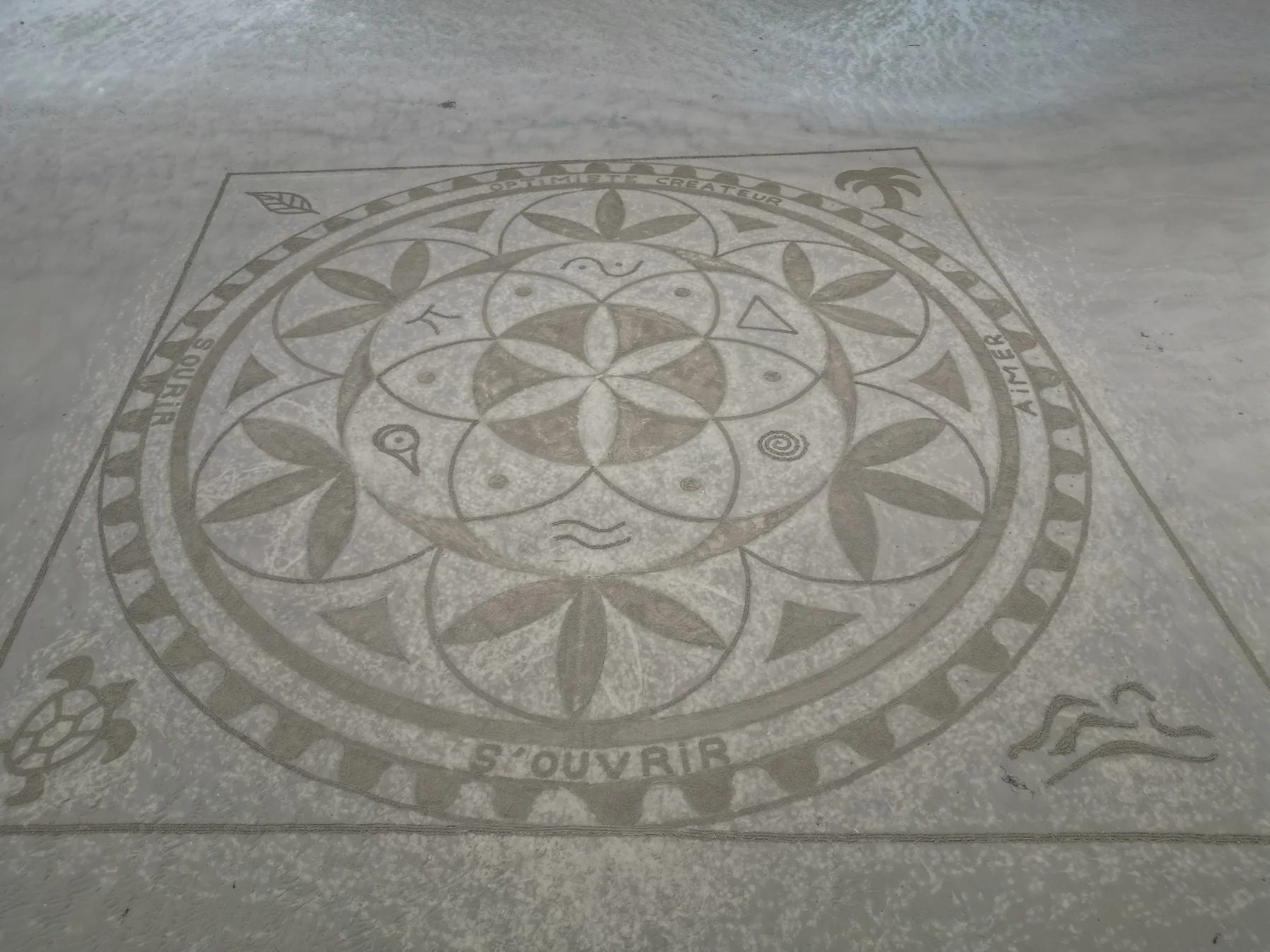 Grand mandala circulaire composé de motifs floraux et symboliques tracé dans le sable