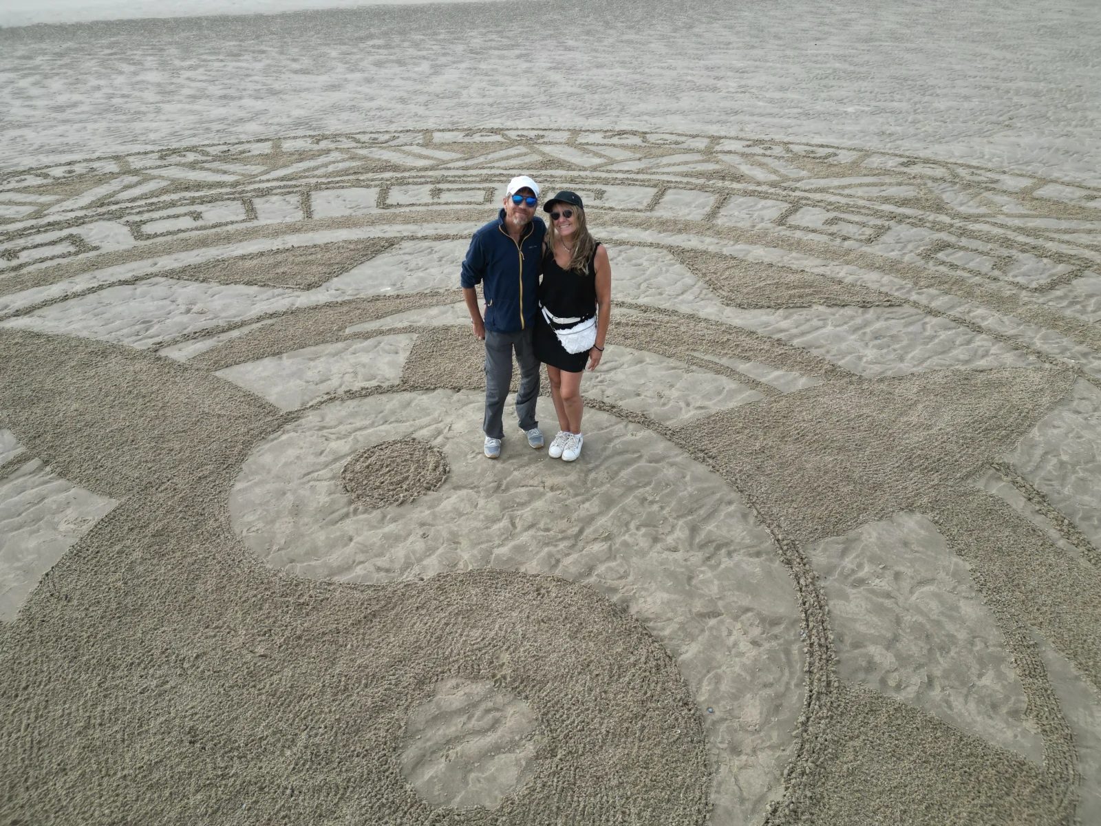 Deux personnes au centre d’un vaste mandala géométrique tracé sur la plage