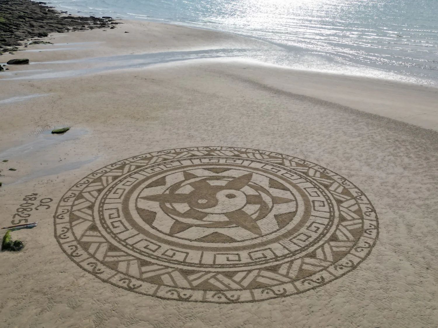 Mandala circulaire aux motifs géométriques tracé dans le sable près de la mer