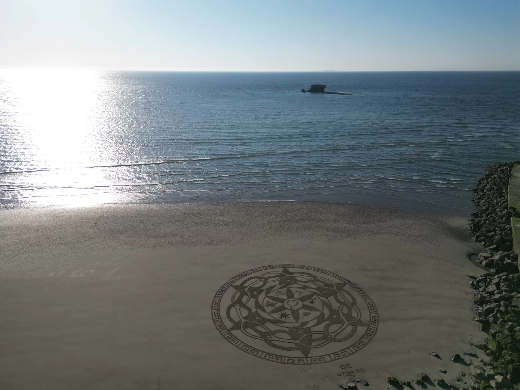Mandala circulaire au pied d’une vaste étendue de mer éclairée par le soleil