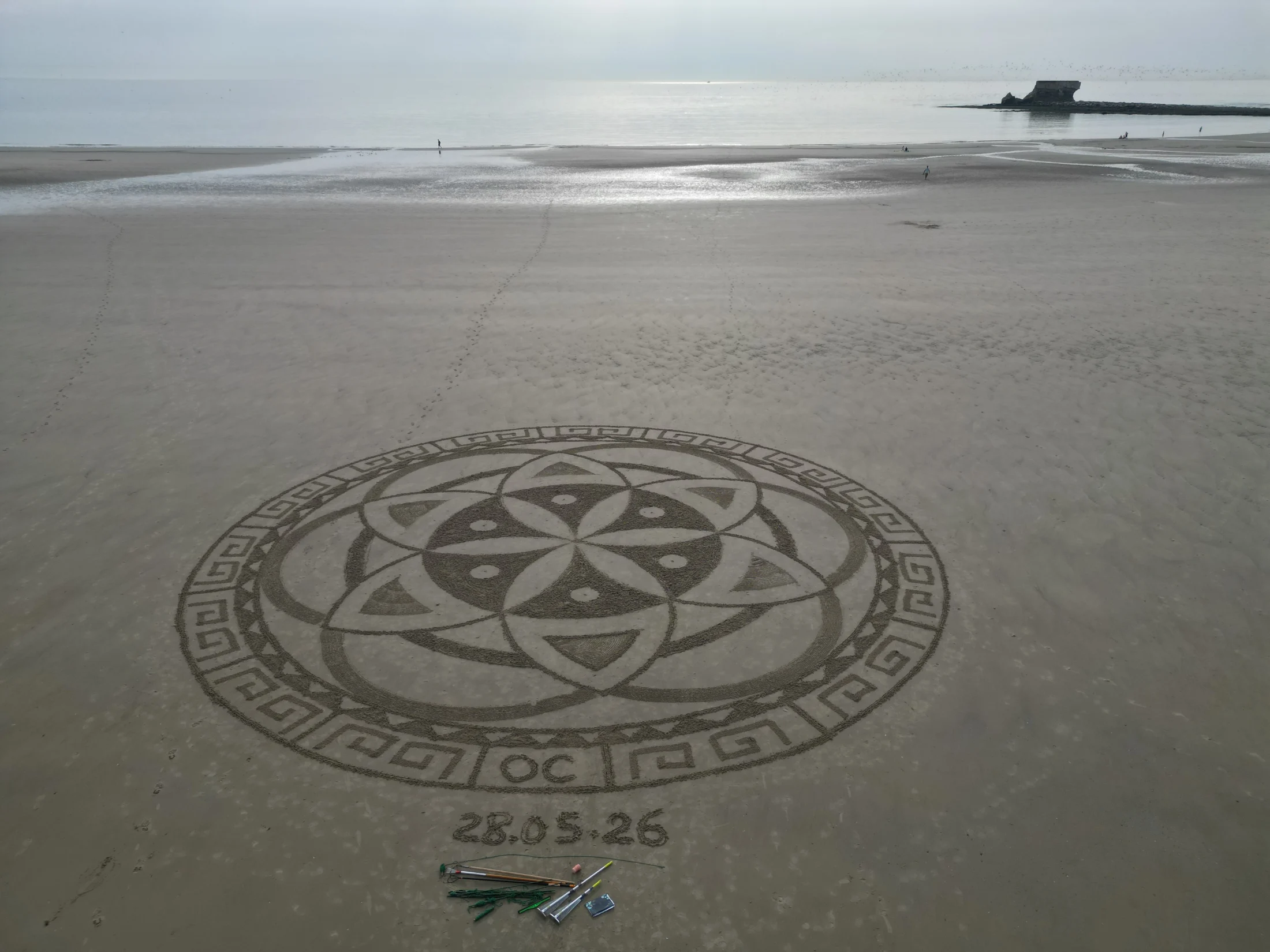 Grand mandala circulaire tracé dans le sable face à la mer
