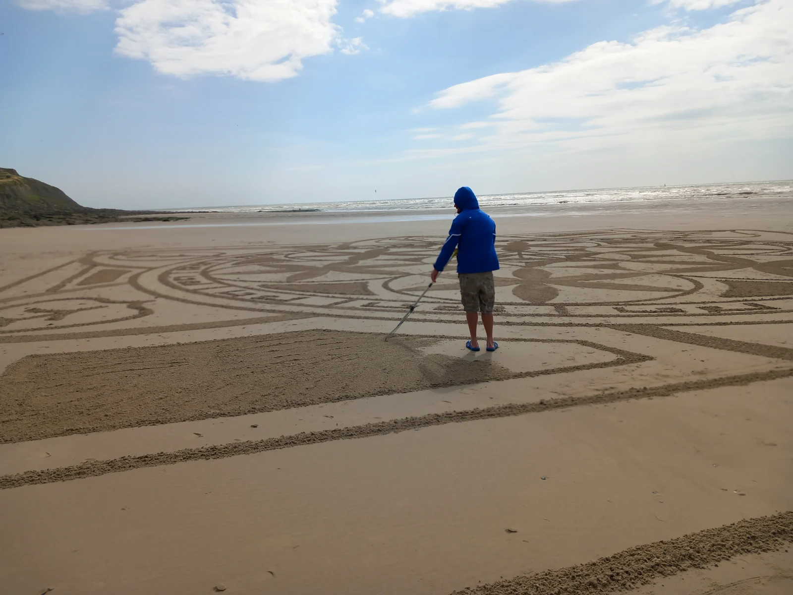 Créateur ajustant les détails d’un grand mandala presque achevé sur la plage