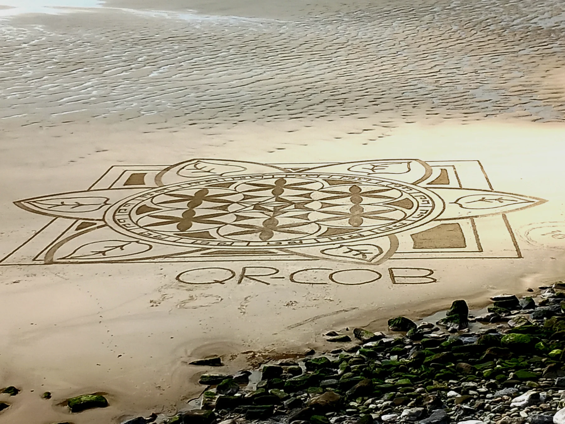 Vue finale en hauteur d’un grand mandala achevé tracé dans le sable au bord de la mer