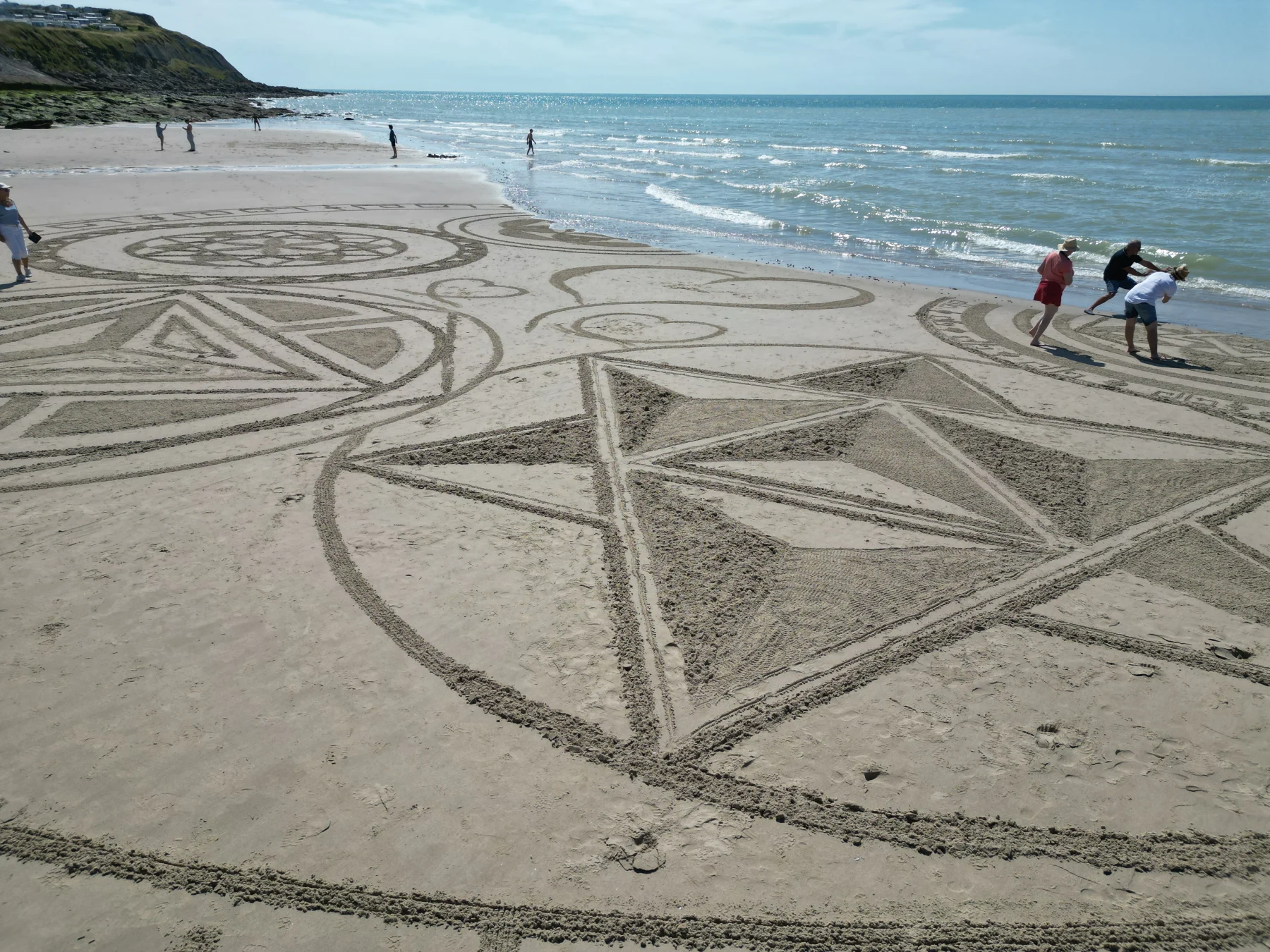 Participants réalisant ensemble une grande création géométrique tracée dans le sable
