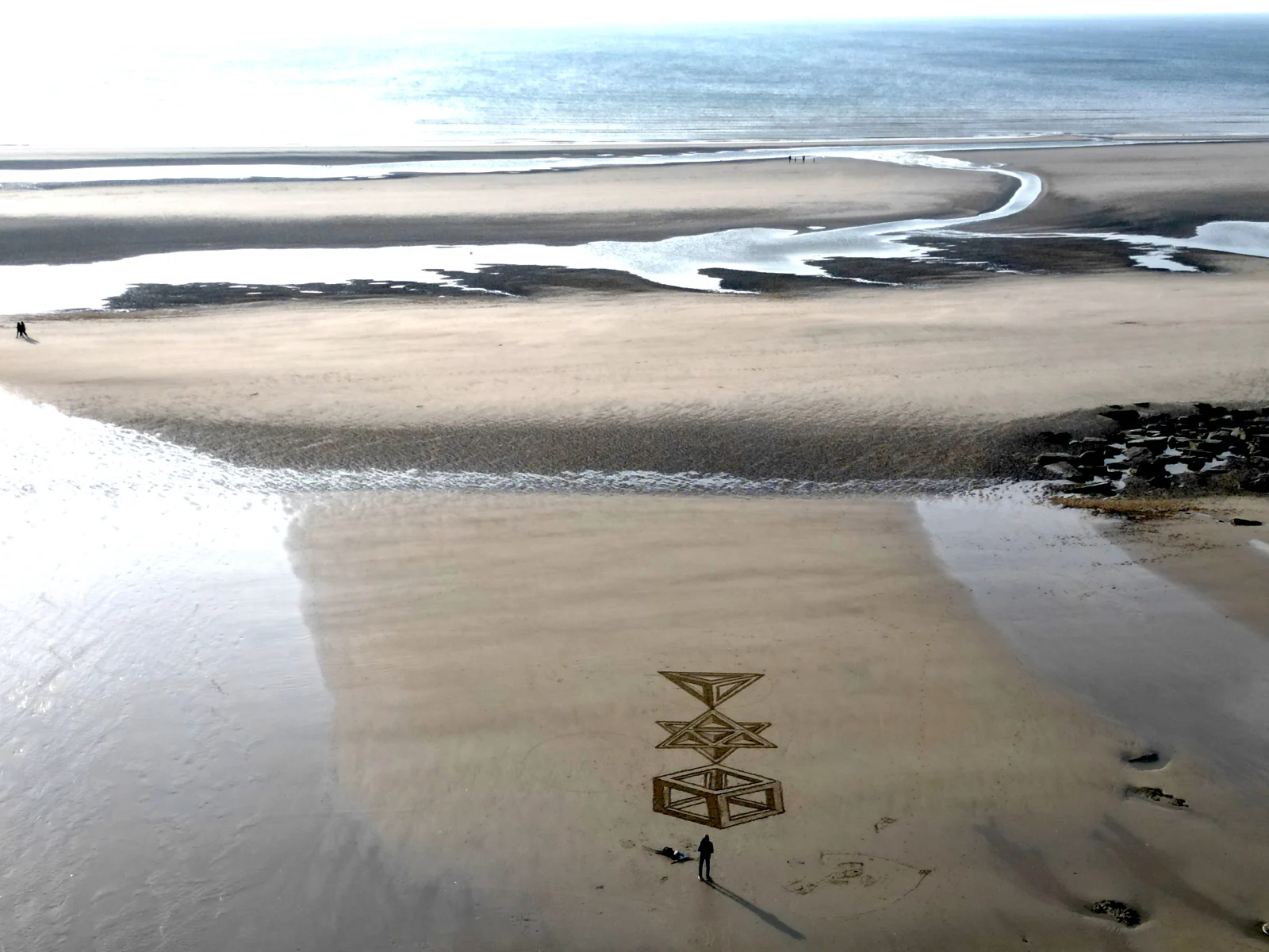 Composition géométrique monumentale tracée sur une vaste plage avec une personne pour échelle