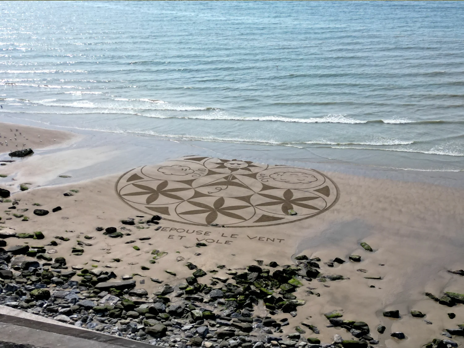 Mandala circulaire tracé sur une plage rocheuse au bord de la mer
