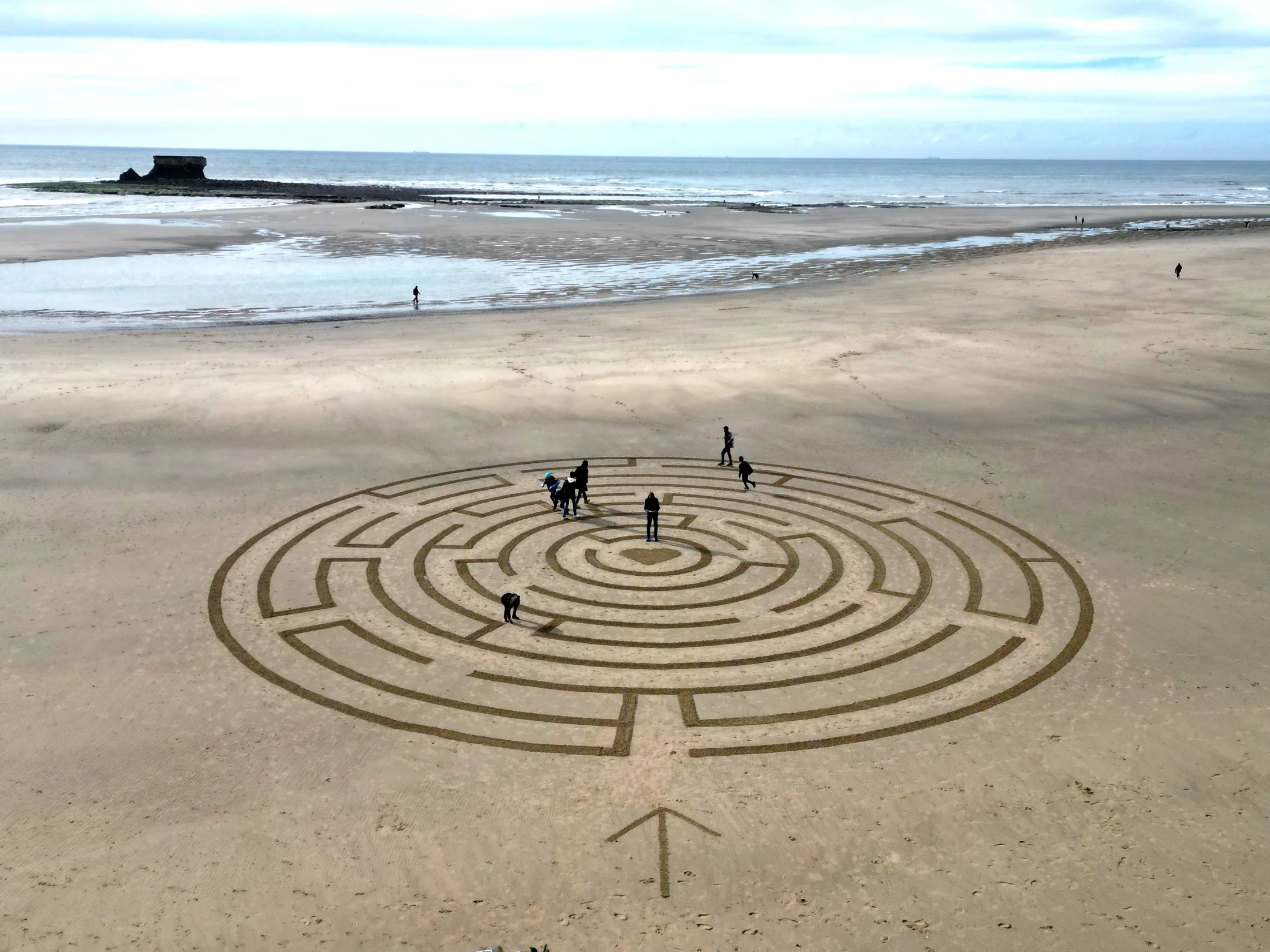 Grand labyrinthe tracé dans le sable avec plusieurs participants face à la mer