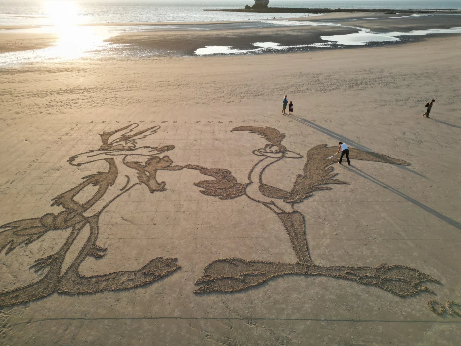 Grande fresque figurative tracée dans le sable avec des personnes donnant l’échelle de l’œuvre