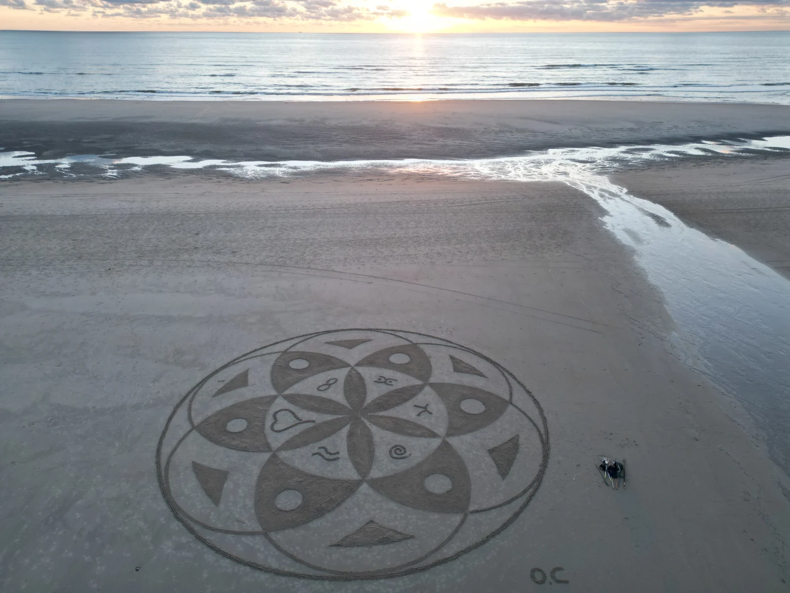 Mandala tracé dans le sable au coucher du soleil face à la mer