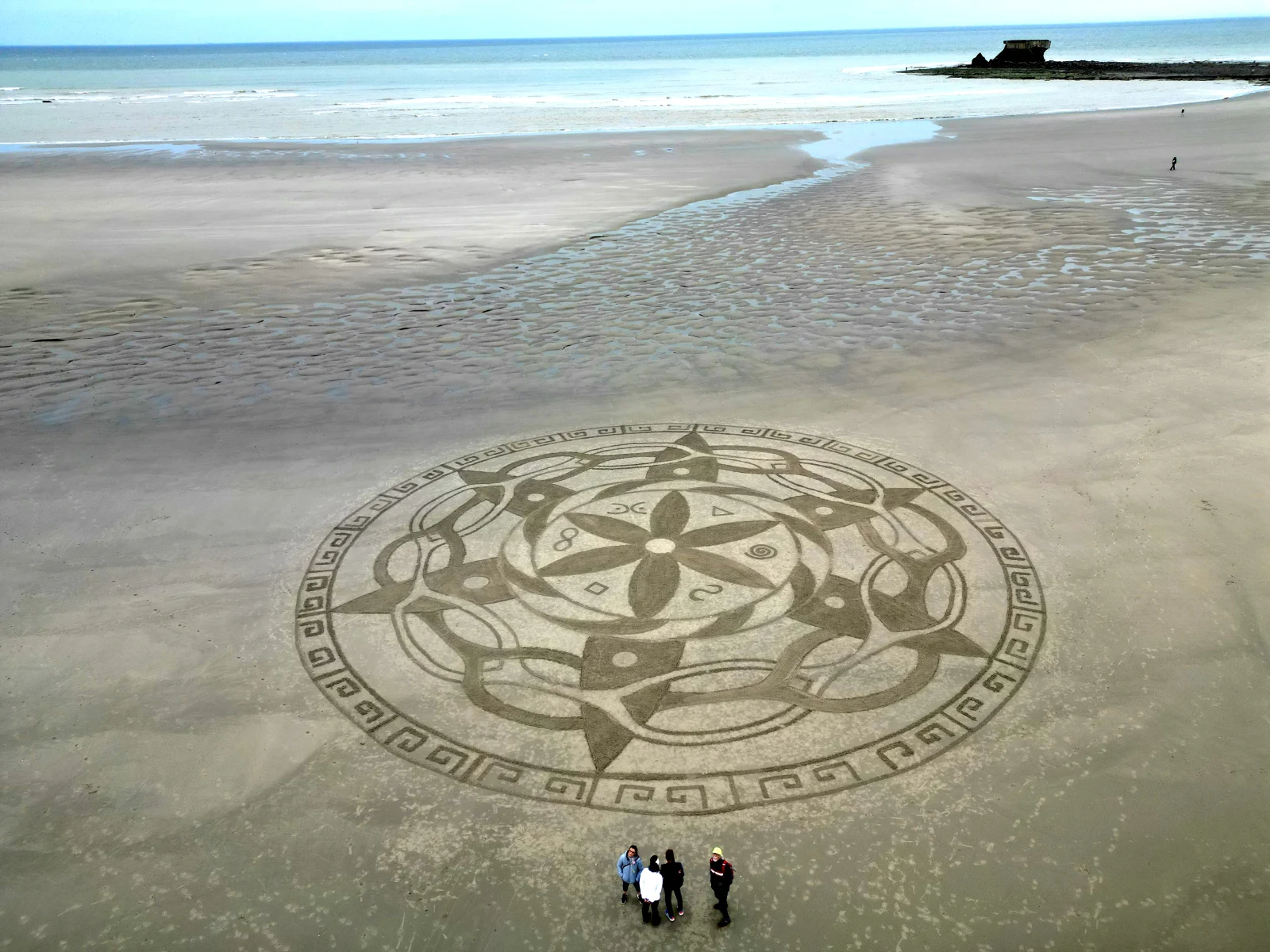 Grand mandala circulaire tracé dans le sable au bord de la mer