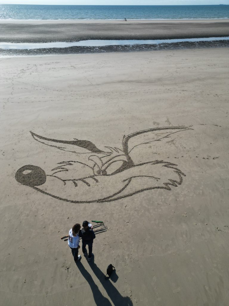 Vue aérienne du visage de Coyote tracé dans le sable, avec deux personnes près du dessin