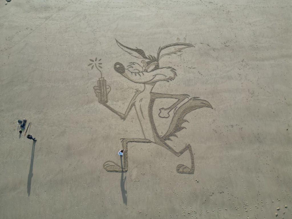 Fresque complète de Coyote tracée dans le sable, avec des personnes donnant l’échelle