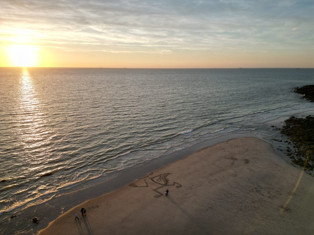 Vue panoramique de la plage et de la mer au soleil couchant, avec la fresque Coyote dans le sable